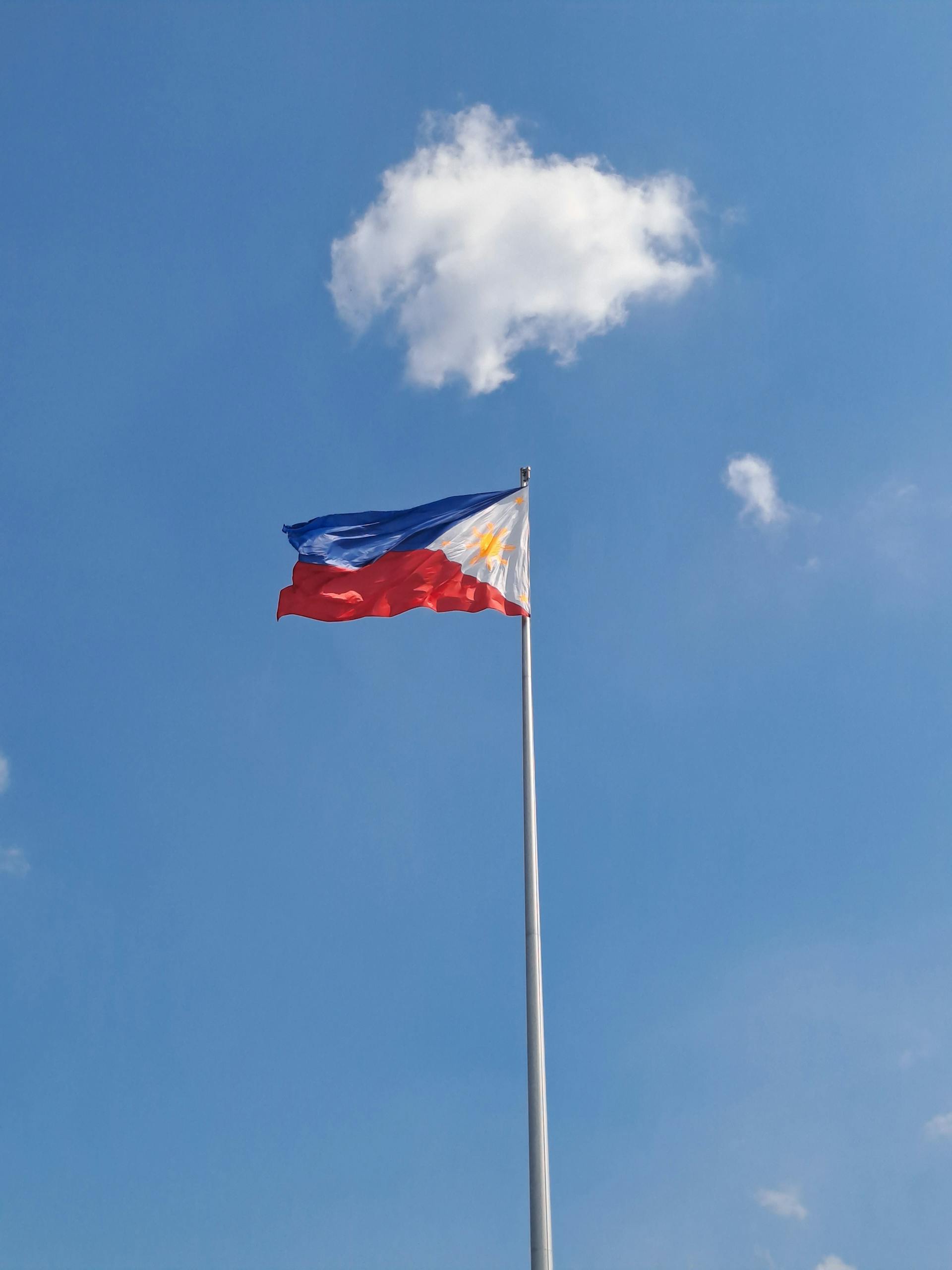 The Philippine flag waving proudly against a vibrant blue sky in Manila.